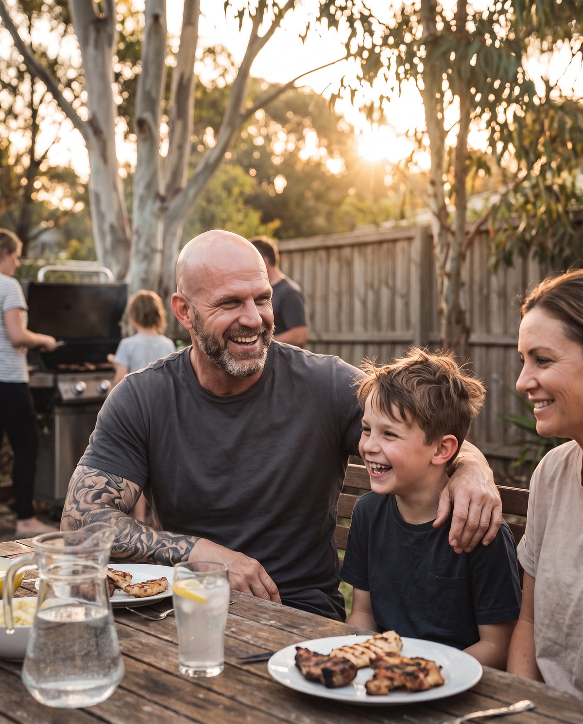 A man laughing with his son and partner at a backyard family barbecue