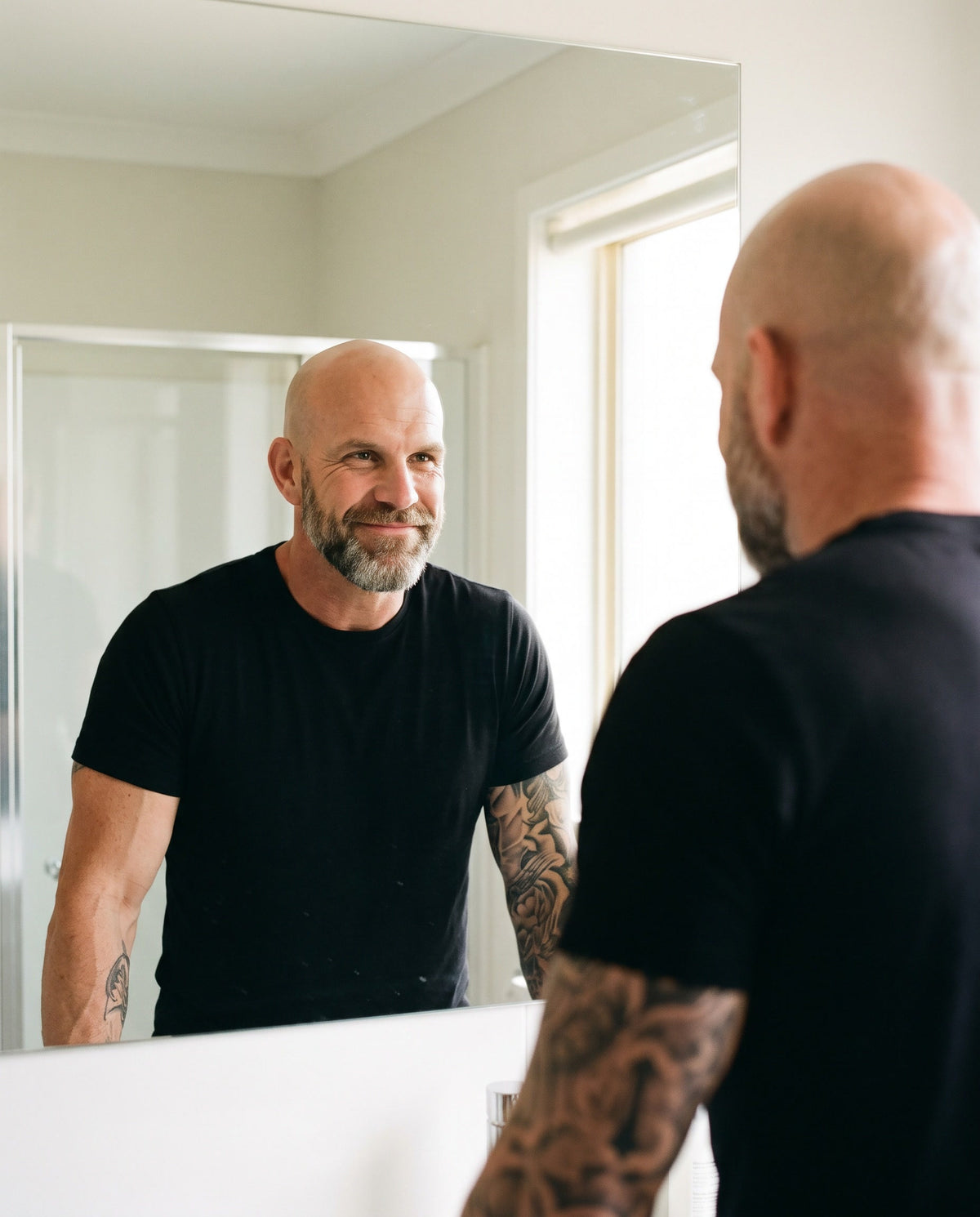 A man looking at his reflection in the mirror with a calm, proud smile