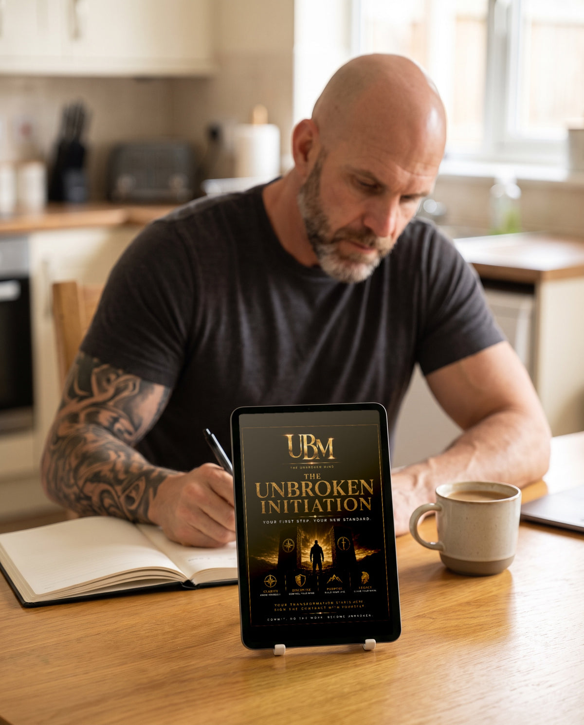The Unbroken Initiation on a tablet at a sunny kitchen table while a man writes notes behind it
