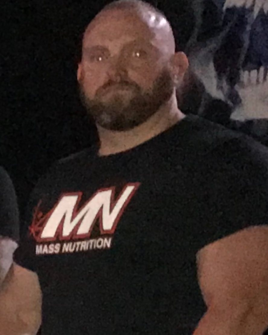 Standing at an event in a black T-shirt, arms relaxed at the sides.