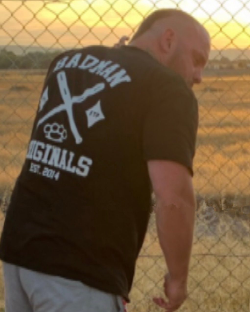 Seen from behind at a wire fence, looking out over a dry paddock at sunset.